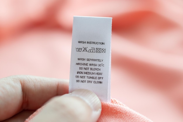 Tenere in mano e leggere al bucato bianco istruzioni per il lavaggio etichetta dei vestiti sulla camicia rosa