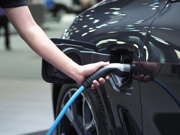 Tenere in mano la spina del veicolo di ricarica elettrica per ricaricare la batteria dell'energia pulita di colore nero dell'auto