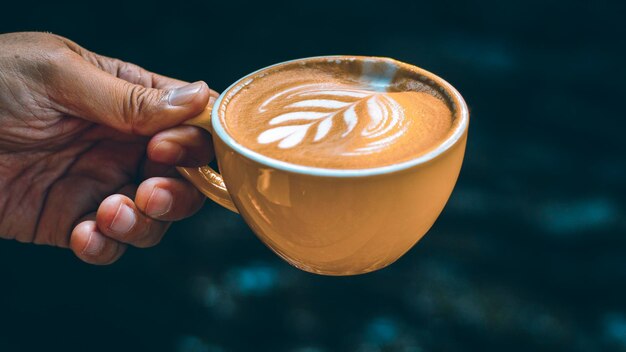 Tenere in mano la tazza Hot Latte Art in tazza gialla su sfondo scuro.