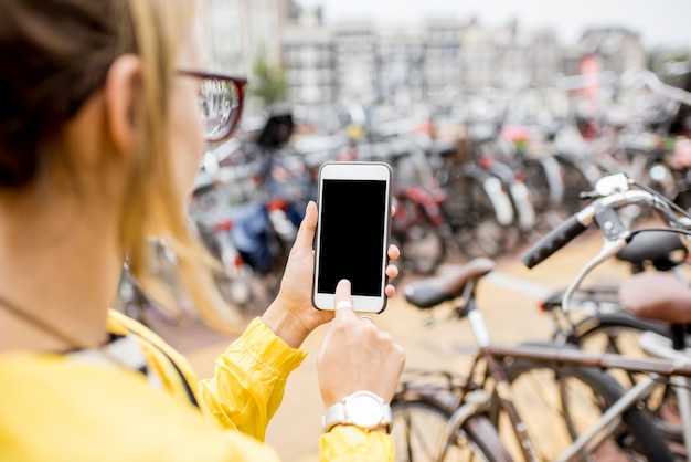 Tenere in mano uno smartphone con schermo vuoto per copiare e incollare sullo sfondo del parcheggio delle biciclette