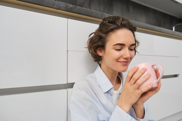 Tenerezza e relax la giovane donna beve caffè e sorride rilassata con una tazza di tè si siede su kitch