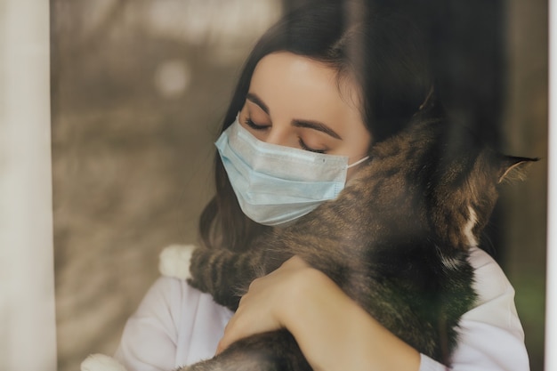 Teneri abbracci di una ragazza con un gatto vicino alla finestra.