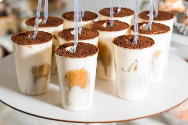 Tenero tiramisù in bicchieri di plastica con cucchiai di plastica Porzioni di dolce italiano al candy bar