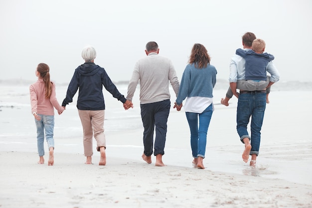 Tenersi per mano camminando e una grande famiglia sulla spiaggia per fare esercizio durante le vacanze estive Nonni genitori e bambini in una passeggiata all'aperto nella natura in riva all'oceano mentre sono in vacanza avventura o viaggio