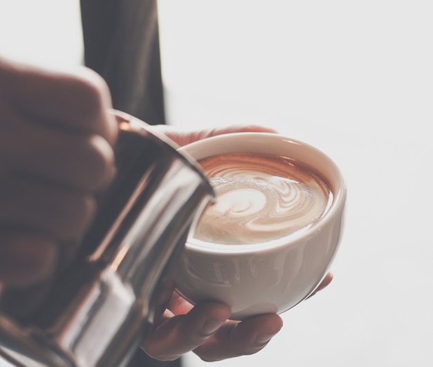 tenuta maschio del barista e latte di versamento per preparare la tazza di caffè