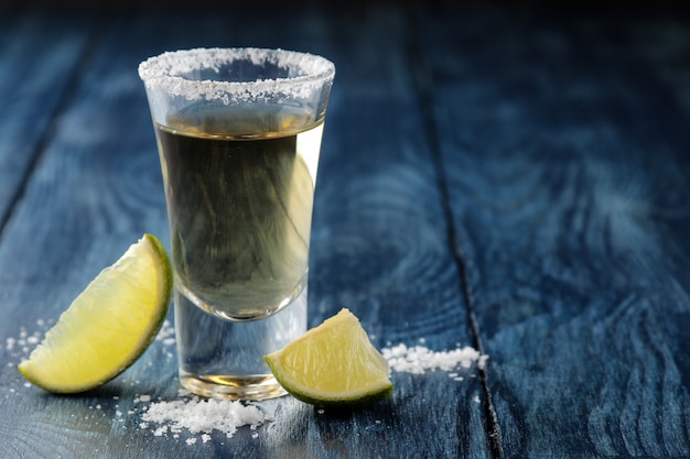 Tequila dell'oro in vetro con sale e calce su fondo di legno blu