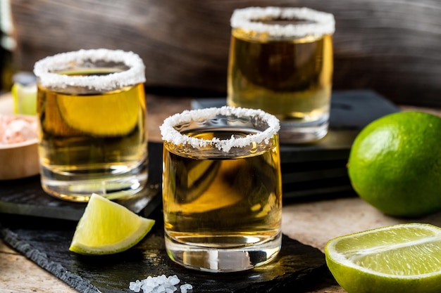 Tequila messicana d'oro con lime e sale su fondo di legno rustico Concetto di bevanda alcolica Bevanda nazionale messicana Primo piano