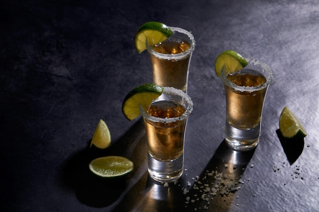 Tequila messicana d'oro con lime e sale su fondo rustico scuro Concetto di bevanda alcolica. Tequila s