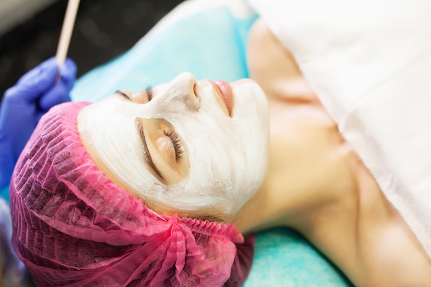 Terapia della stazione termale per la giovane donna che ha maschera facciale al salone di bellezza.