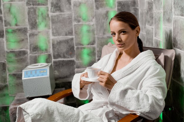 Terapia inalatoria nella stanza del sale nella spa. Giovane donna con una tazza di tè rilassante.