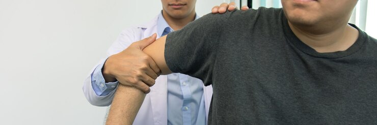 Terapis fisik menekan bahu pasien untuk memeriksa rasa sakit
