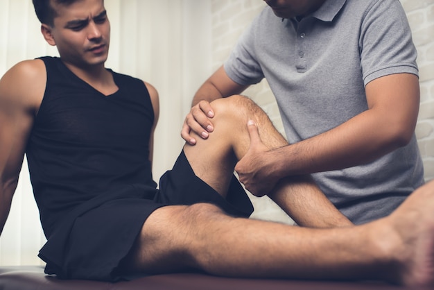 Terapista che cura ginocchio ferito del paziente maschio dell'atleta in clinica