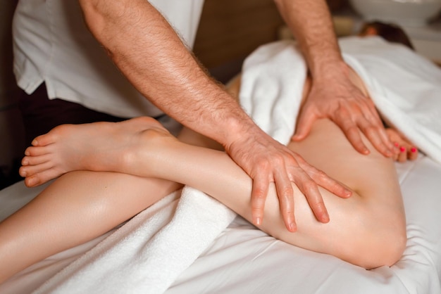 Terapista di massaggio che massaggia la gamba femminile al salone della stazione termale