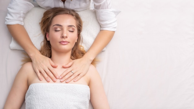 Terapista femminile che guarisce una ragazza sdraiata con il tocco delle sue mani su uno sfondo bianco.