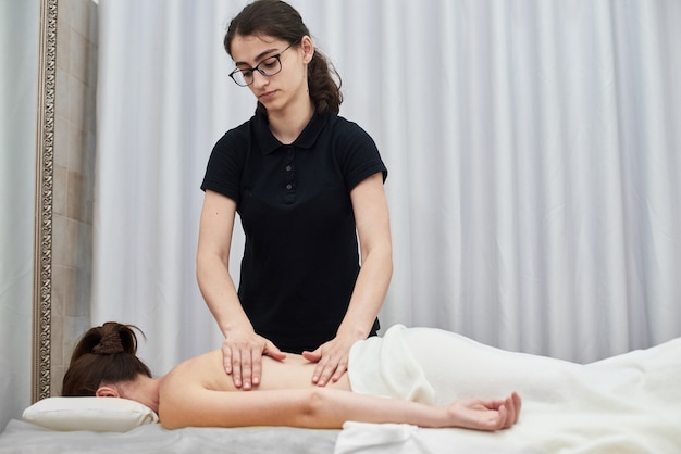 Terapista femminile massaggia una giovane donna sulla schiena e sulle spalle Massaggio rilassante