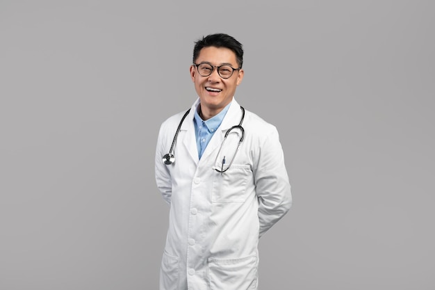 Terapista maschio asiatico invecchiato centrale bello fiducioso allegro in vetri del camice bianco con lo stetoscopio