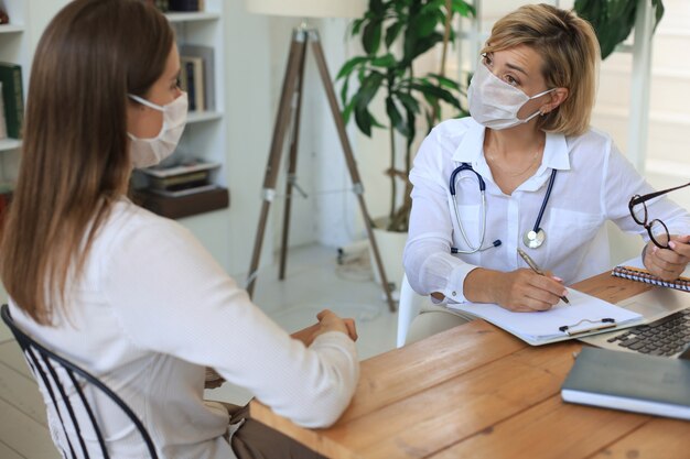 Terapista medico femminile di mezza età in maschera medica su consultazione con il paziente in ufficio.