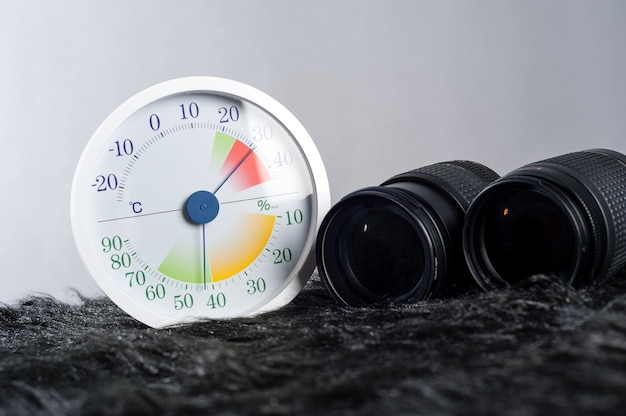 Termometro analogico bianco e igrometro con attrezzatura fotografica.