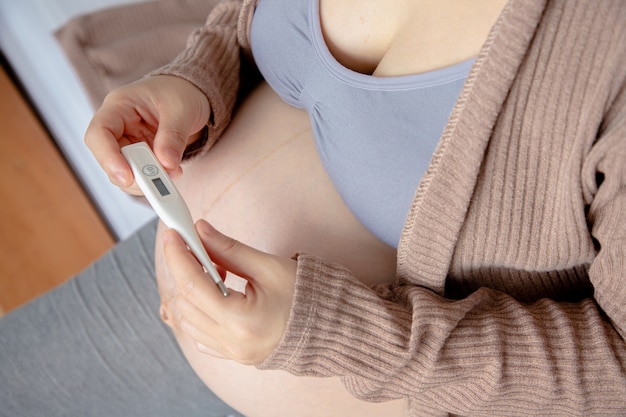 Termometro digitale della giovane tenuta della donna incinta.