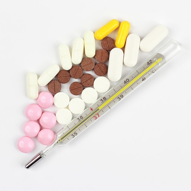 Termometro e pillole mediche su sfondo bianco. farmacologia, medicina e cura delle malattie