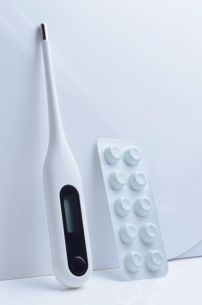 termometro elettronico e pillole su sfondo bianco. concetto.