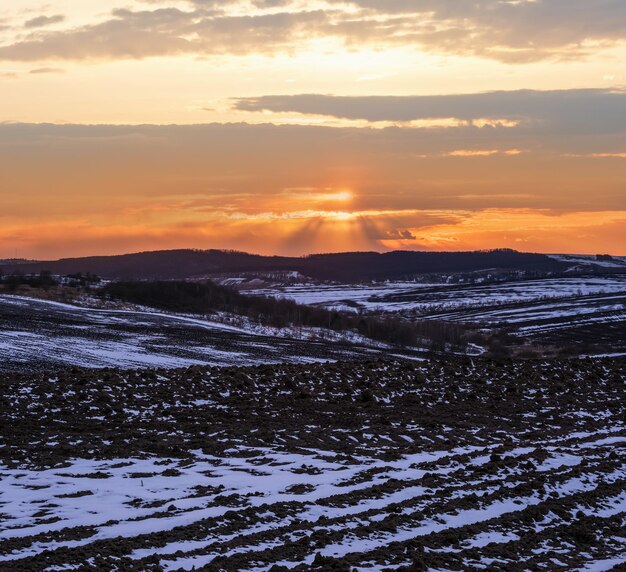 Terra coltivabile di terra nera coperta dall'ultima neve all'inizio della primavera Calmo tramonto serale nella campagna ucraina della regione di Lviv