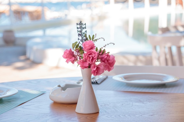 Terrazza estiva del ristorante Sui tavoli posati piatti bianchi bicchieri fiori tropicali rosa