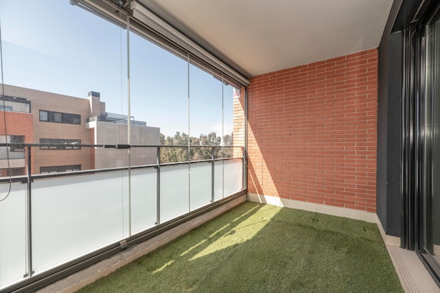 Terrazza vetrata con parete in mattoni con pavimento in erba artificiale e vista sulla città
