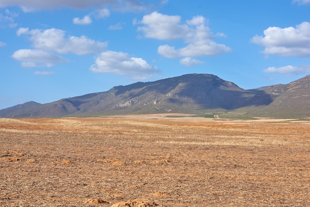 Terreni agricoli dopo il raccolto Terreni agricoli nel Capo Occidentale del Sud Africa a metà giornata Una montagna in una terra brulla con un cielo azzurro nuvoloso Una fattoria vuota con vista sulla natura e uno spazio di copia