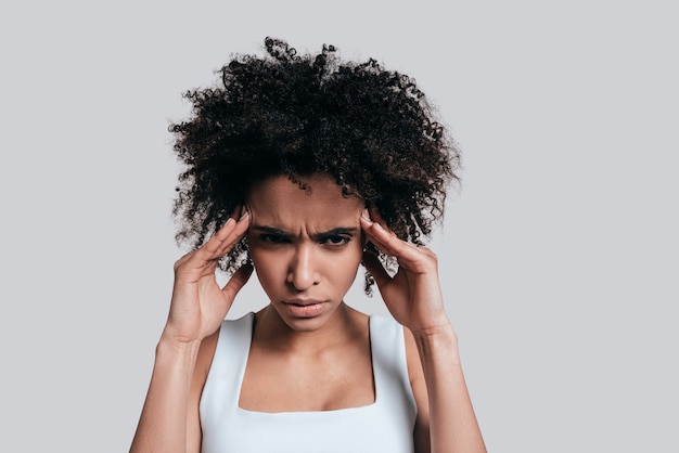 Terribile mal di testa. Giovane donna africana frustrata in abbigliamento casual che si tocca la testa con le mani