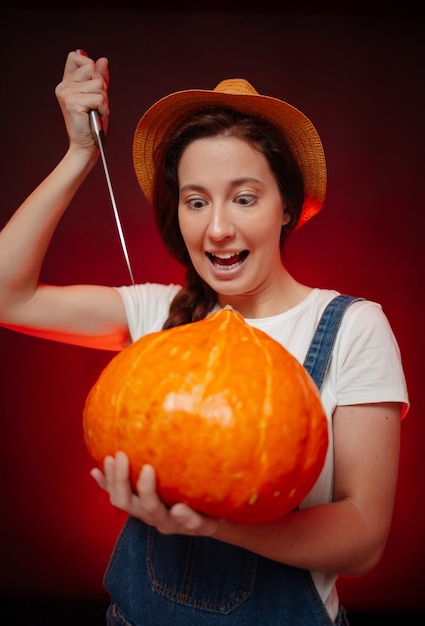 Terrificante donna contadina su uno sfondo rosso scolpisce una faccia su un concetto di zucca di festa di halloween