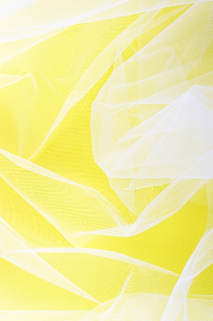 Tessuto in tulle trasparente disposto in morbide pieghe su sfondo giallo fuoco selettivo
