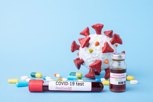 Test Covid-19 positivo e vaccino vicino a diverse pillole e primo piano del modello di coronavirus su un blu