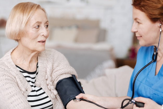 Test regolari a casa. Un operaio medico ordinato e grazioso paga una visita al suo paziente per condurre un esame e prendersi cura di una signora anziana