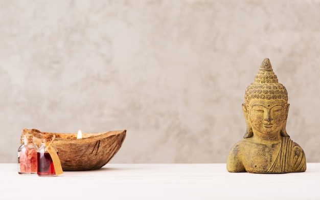 Testa di Buddha e candela con olio aromatico e sale marino su sfondo chiaro. Spa, meditazione, relax e concetto di aromaterapia.