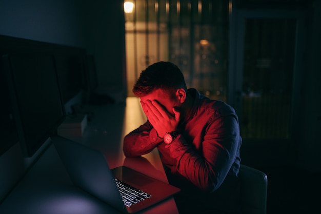 Testa triste della tenuta del lavoratore in mani mentre sedendosi tardi nell'ufficio alla notte.