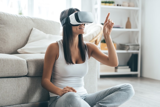 Testare nuove tecnologie. Attraente giovane donna in cuffia VR che gesticola e sorride mentre è seduta a casa