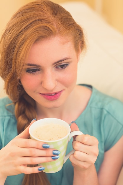 Testarossa sorridente che si siede sullo strato che mangia caffè