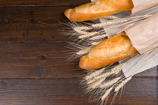 Teste di semi di gambo di grano intero essiccate tra due deliziosi amori di pane francese in sacchetti di carta sul tavolo marrone scuro