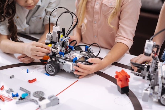 Testing tech invention together. Smart confident involved schoolchildren sitting at school and testing cyber toy while having science lesson