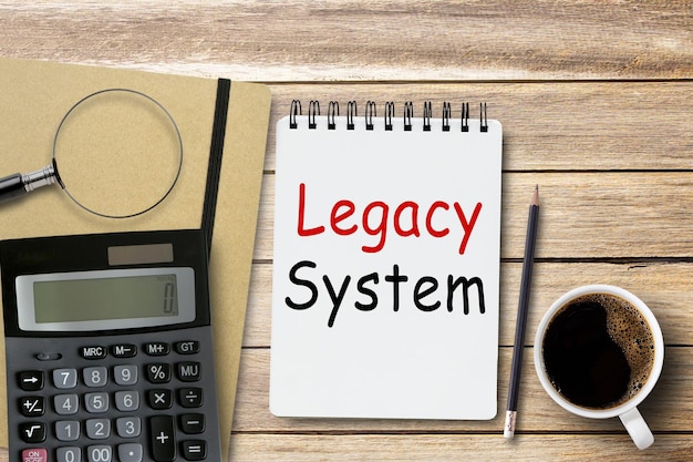 Testo del sistema legacy sul taccuino sullo sfondo del posto di lavoro della scrivania dell'ufficio