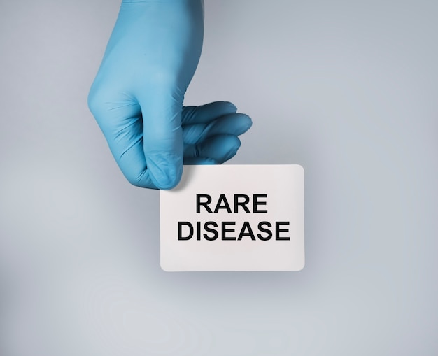 Testo di concetto di malattia rara su carta bianca in mani in guanti blu