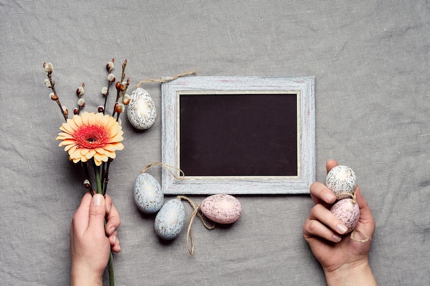 Testo di decorazioni di Pasqua Buona Pasqua sulla lavagna Lavagna Mani che tengono mazzo di fiori con gerbera e salice e legno Uova di Pasqua Sfondo tessile lino colorato terra