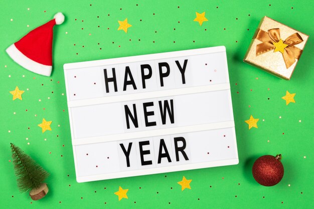 Testo di felice anno nuovo in una scatola leggera, decorazioni e glitter su sfondo verde
