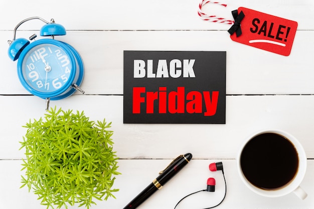 Testo di vendita di Black Friday sull&#39;etichetta rossa e nera con gli accessori dell&#39;ufficio sulla tavola di legno bianca