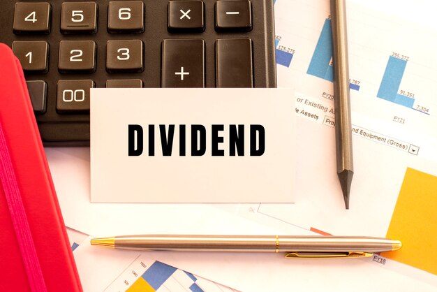 Testo DIVIDEND su carta bianca con penna in metallo, calcolatrice e grafici finanziari financial