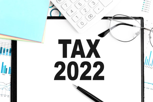 Testo TAX 2022 su appunti, penna, occhiali, calcolatrice, adesivo, grafico. Concetto di affari. Disposizione piatta.