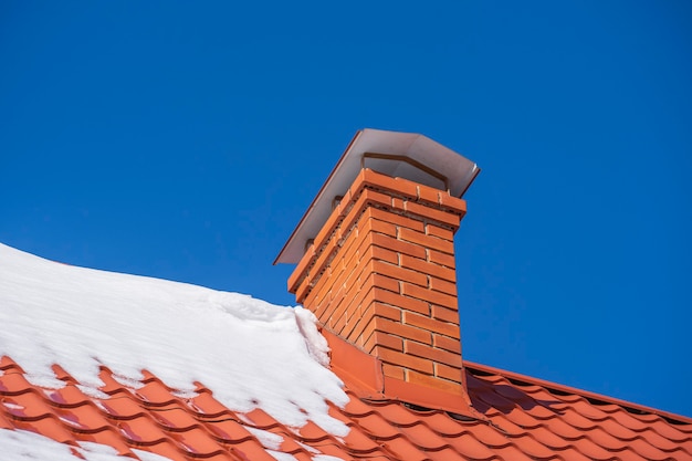 Tetto rosso di una casa unifamiliare e camino e neve contro il cielo azzurro in inverno, primo piano