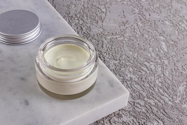 Texture delicate di olive o aloe vera nutrienti in un barattolo di vetro cosmetico su un podio di marmo bianco e un cemento grigio Un imballaggio di layout di spazio di copia