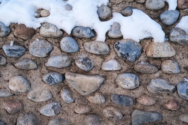 Texture di pietre di ciottoli nel vecchio muro di cemento in inverno con la neve